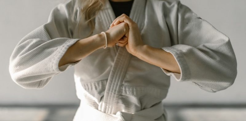 Close-up of a karate practitioner in white gi performing a hand gesture indoors.