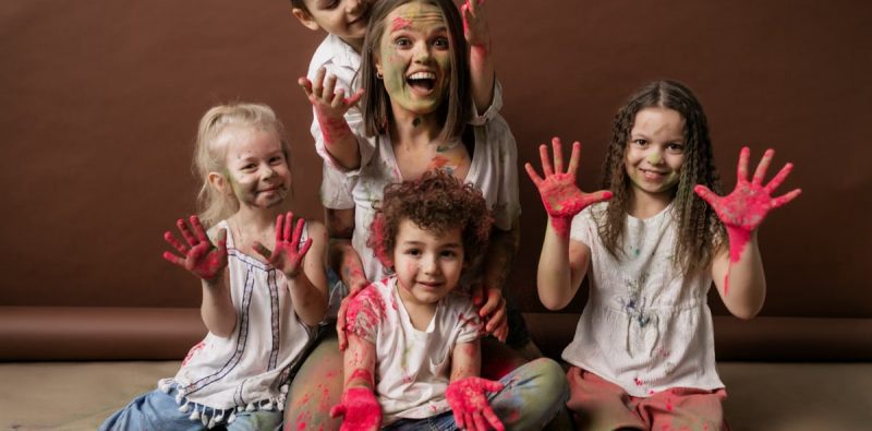 A happy group of children and woman covered in colorful powder, all smiles and joy.